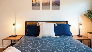 A hotel room with a large bed, two nightstands, a wall-mounted lamp, and three framed pictures above the bed.