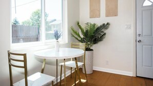 A dining area with a round table, four chairs, a potted plant, and two wall-mounted artworks.