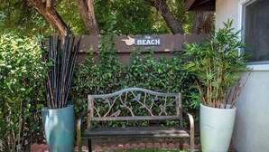 A bench with a decorative backrest, surrounded by lush greenery and a sign indicating a direction to the beach.