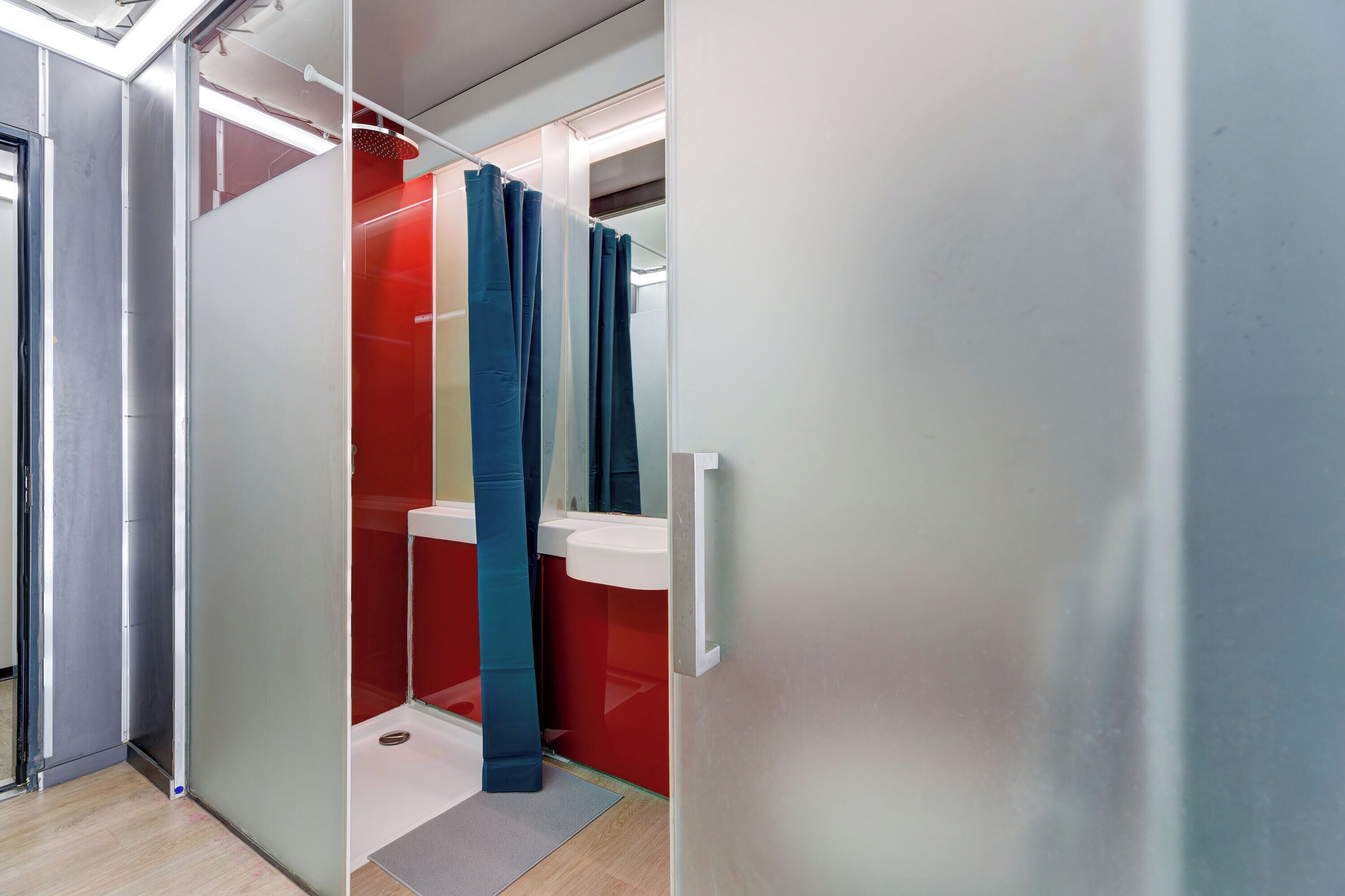Ein modernes Badezimmer mit Glastrennwand, einem roten Waschbecken und einem blauen Duschvorhang.