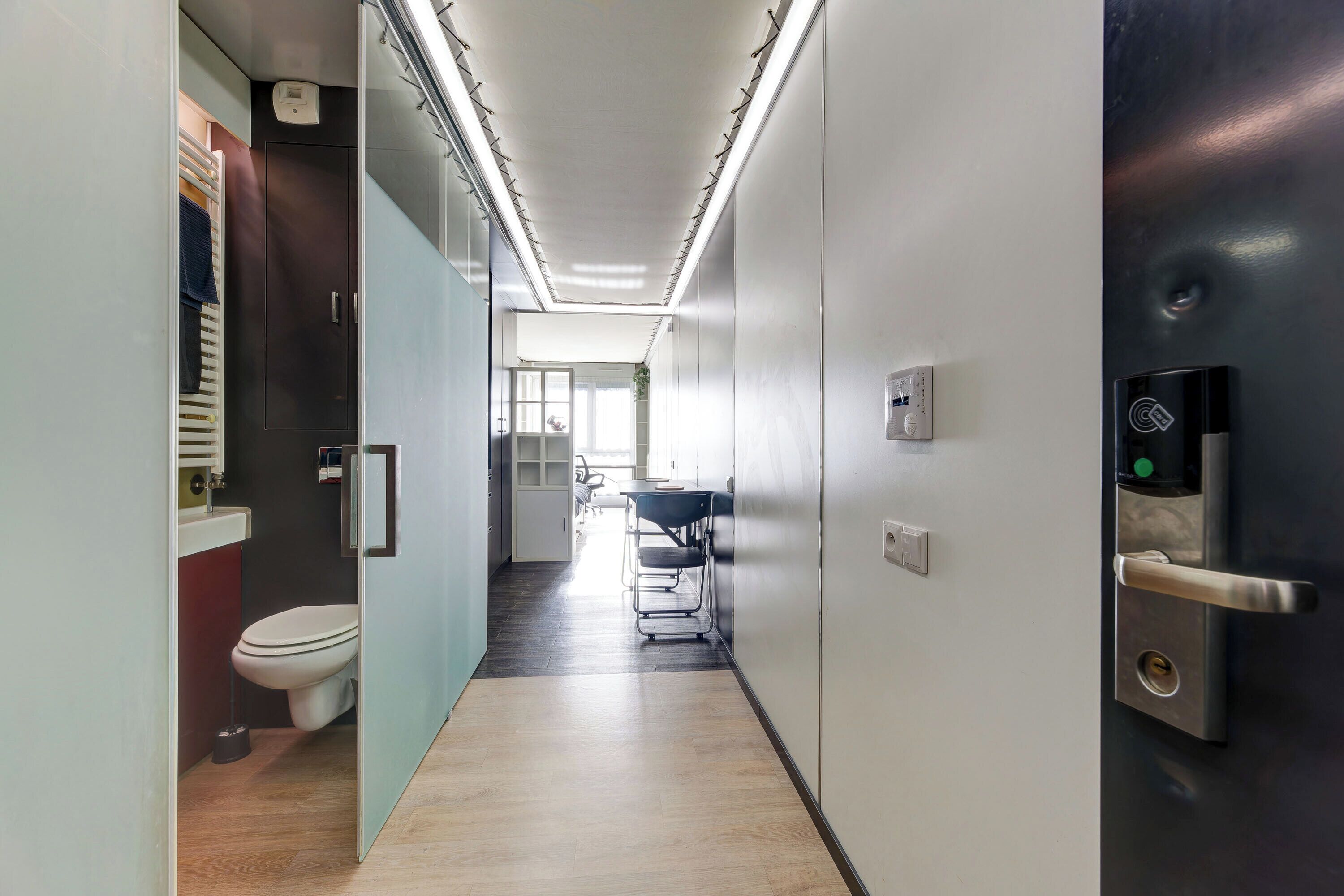 A modern hallway with a toilet, a sink, and a door with a keypad lock.