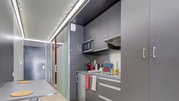 A compact kitchen with grey cabinets, a microwave, a sink, and a small countertop. - 40 - Le Lokup - Wifi - Proche tram (Reims)