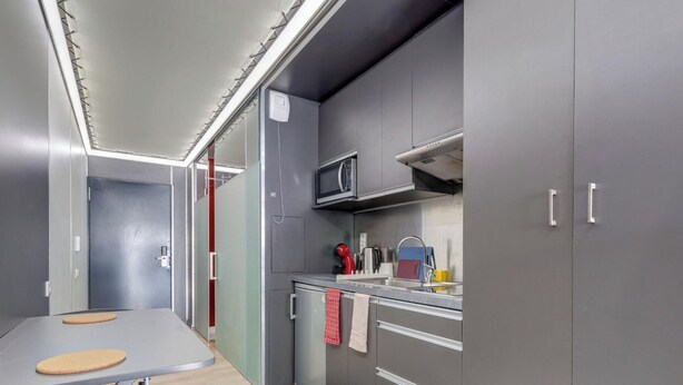 Una cocina compacta con armarios grises, un microondas, un lavabo y una pequeña encimera.