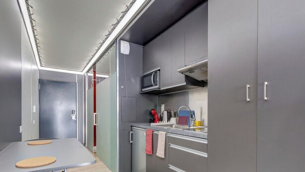 A compact kitchen with grey cabinets, a microwave, a sink, and a small countertop. - 30 - Le Lokup - Wifi - Proche tram (Reims)