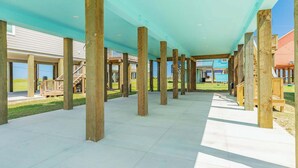 Un espacio al aire libre cubierto con pilares de madera, suelo de baldosas y vista de edificios al fondo.