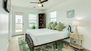 A bedroom with a bed, a nightstand, a ceiling fan, a bookshelf, and a door. - Stunning Surfside Beach House Near The Jetty (Surfside Beach)
