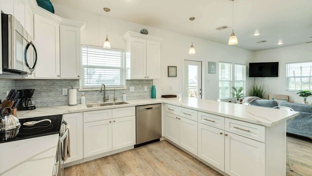 A modern kitchen with white cabinetry, a black stove, and a built-in dishwasher. - Stunning Surfside Beach House Near The Jetty (Surfside Beach)