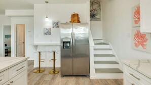A modern kitchen with a stainless steel refrigerator, white cabinetry, and a wooden staircase. - Stunning Surfside Beach House Near The Jetty (Surfside Beach)