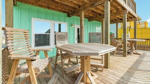 A wooden deck with outdoor seating, including benches and a table, and a green building in the background. - Stunning Surfside Beach House Near The Jetty (Surfside Beach)
