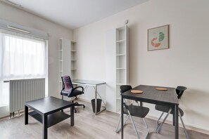 Moderni, pelkistetty huone, jossa on ruokapöytä, tuoleja, patteri, ikkuna, jossa on läpikuultavat verhot, ja seinälle kiinnitetty hylly.