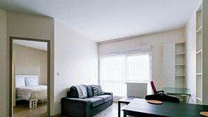Una habitación moderna y luminosa con cama, sofá, mesa de comedor y un amplio ventanal.