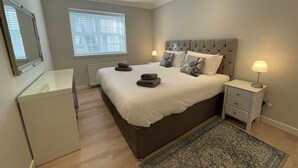 Een slaapkamer met een groot bed, nachtkastjes, een spiegel, een raam met zonwering en een radiator.
