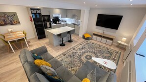 Een moderne woonkamer met een grijze bank, een eettafel en een keuken in de achtergrond.