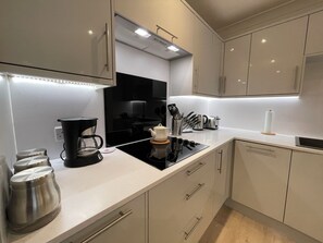 A modern kitchen with white cabinets, a black stove, and stainless steel appliances. - 1 The Maltings, village centre 2 bed 2 bath ground floor apartment, ideal base (Crail)