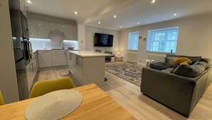 Een modern appartement met keuken, eethoek, woonkamer en een aan de muur bevestigde televisie.
