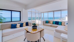 A spacious living area with a large window offering a view of the sea, a sofa set, and a dining table. - Carteia Beachfront at Praia da Gaivota (Loulé)