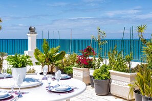 Eine Terrasse mit Esstisch, Kübelpflanzen und Blick aufs Meer.