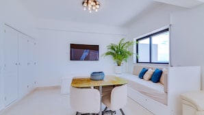 A modern room with a dining table, chairs, a sofa, a TV, and a potted plant. - Carteia Beachfront at Praia da Gaivota (Loulé)
