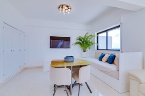 Ein modernes Zimmer mit Esstisch, Stühlen, einer Couch, einem Fernseher und einem Blumentopf.