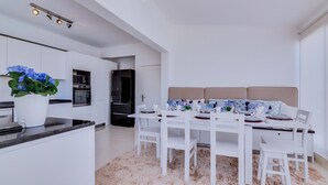 A modern kitchen with white cabinetry, a central island, and a dining area with a white table and chairs. - Carteia Beachfront at Praia da Gaivota (Loulé)