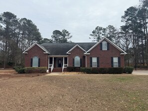 A two-story brick house with a front porch, large windows, and a well-maintained lawn. - Perfect 4-bedroom house in North Augusta (North Augusta)