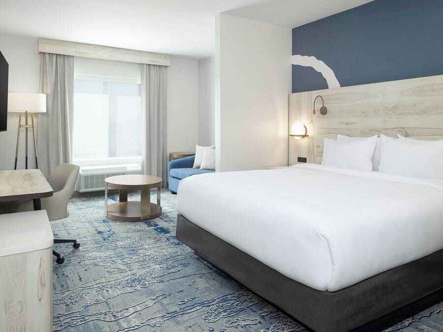 A hotel room with a large bed, a desk, a chair, a round side table, and a window with curtains.