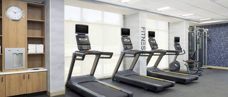 A fitness center with treadmills, a water dispenser, and a clock on the wall.