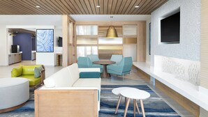 Un hall d’hôtel moderne avec un espace salon, un téléviseur fixé au mur et un coin cuisine en arrière-plan.