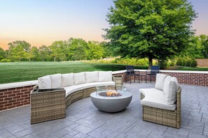 A curved outdoor seating area with a fire pit, wicker furniture, and a view of a grassy field and trees. - Fairfield By Marriott Inn & Suites Athens Madison (Madison)