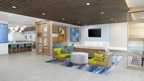 Un intérieur moderne avec un plafond en bois, un téléviseur à écran plat, un coin repas et un espace salon agrémenté d’un pouf rond.