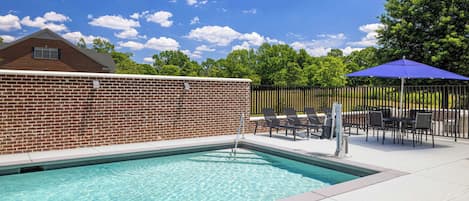 A swimming pool with a brick wall, lounge chairs, and a blue umbrella.