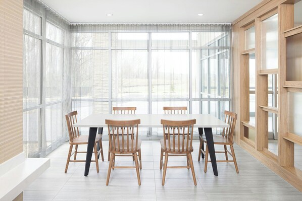 A dining area with a large table and chairs, large windows with sheer curtains, and a wooden wall with built-in shelving. - Fairfield By Marriott Inn & Suites Athens Madison (Madison)