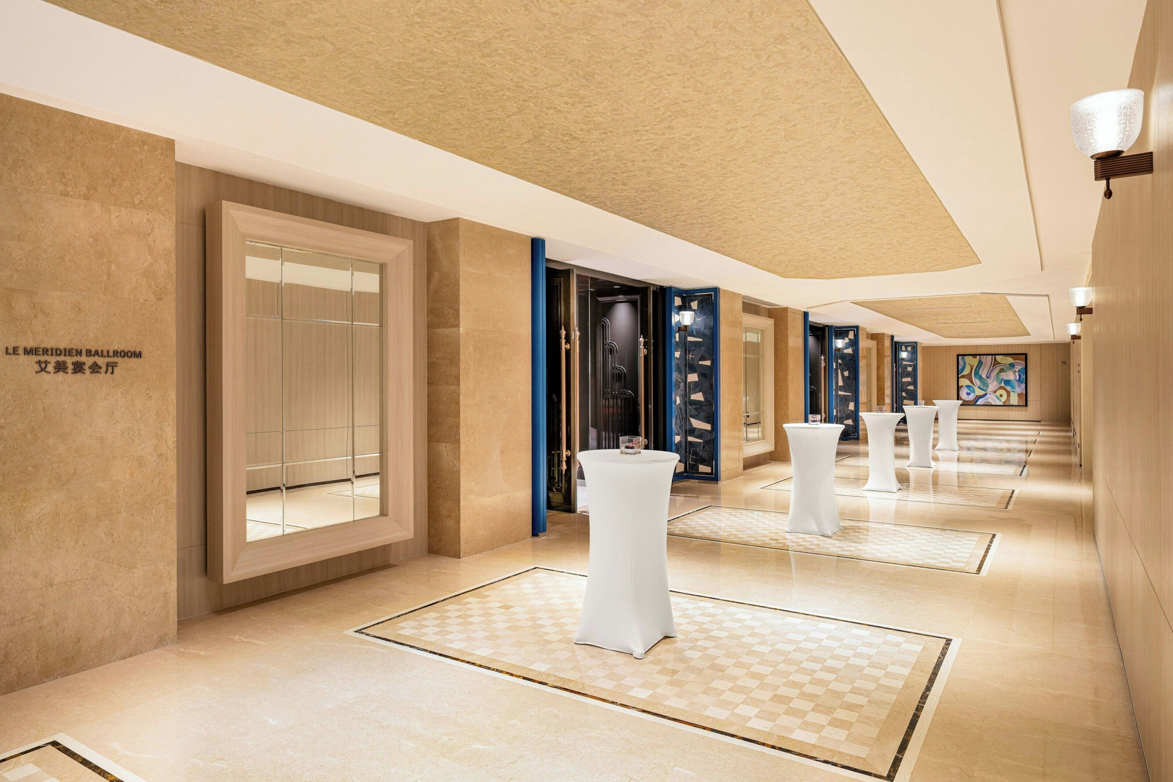 A hotel corridor with a checkered floor, a large mirror, and a sign indicating the ballroom.