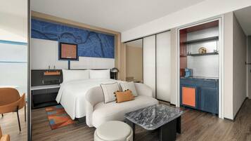 Ein modernes Hotelzimmer mit Bett, Schreibtisch, Sitzecke und einer Küchenzeile.