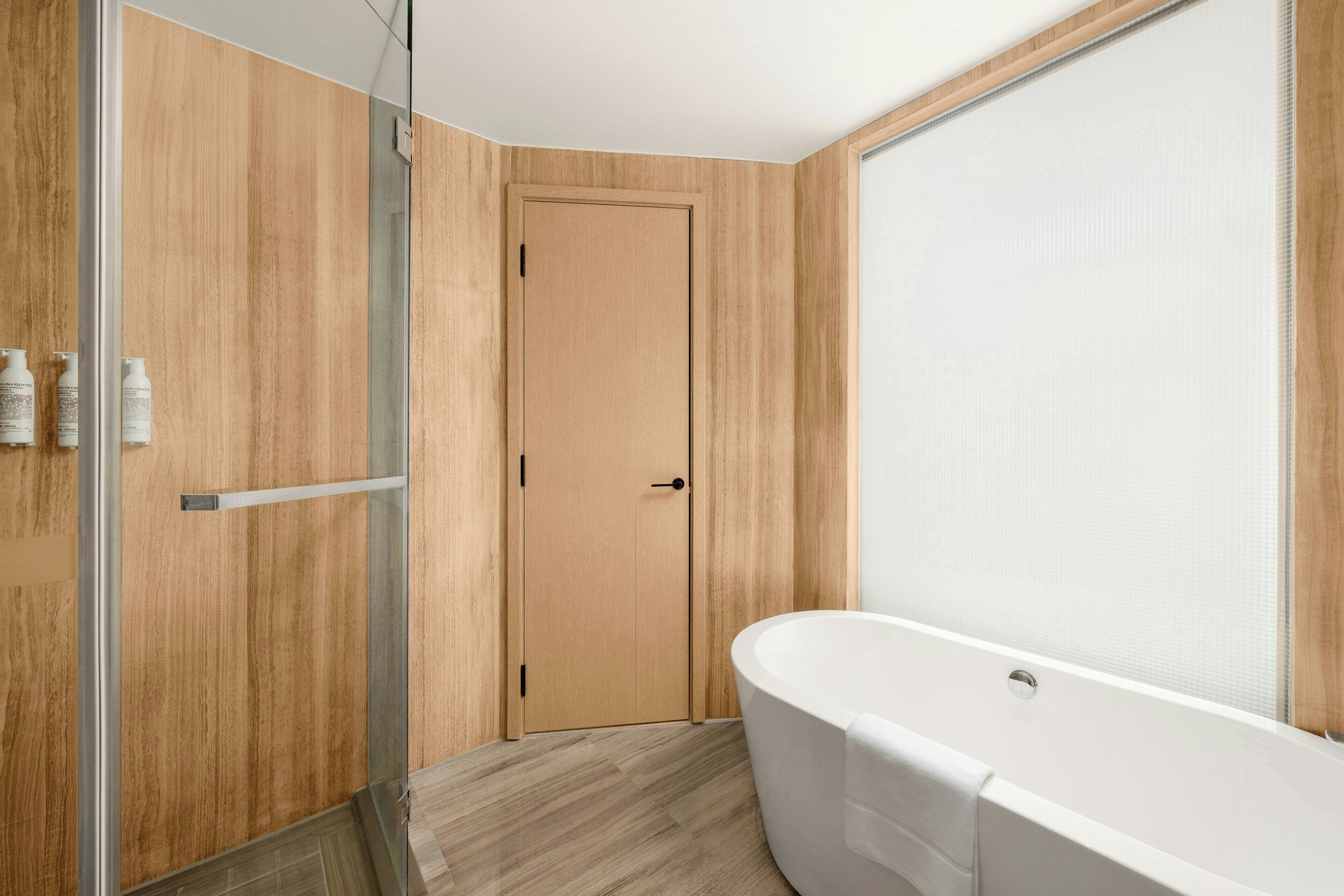 Een moderne badkamer met een vrijstaand bad, houten paneelwanden en een douchecabine van glas.