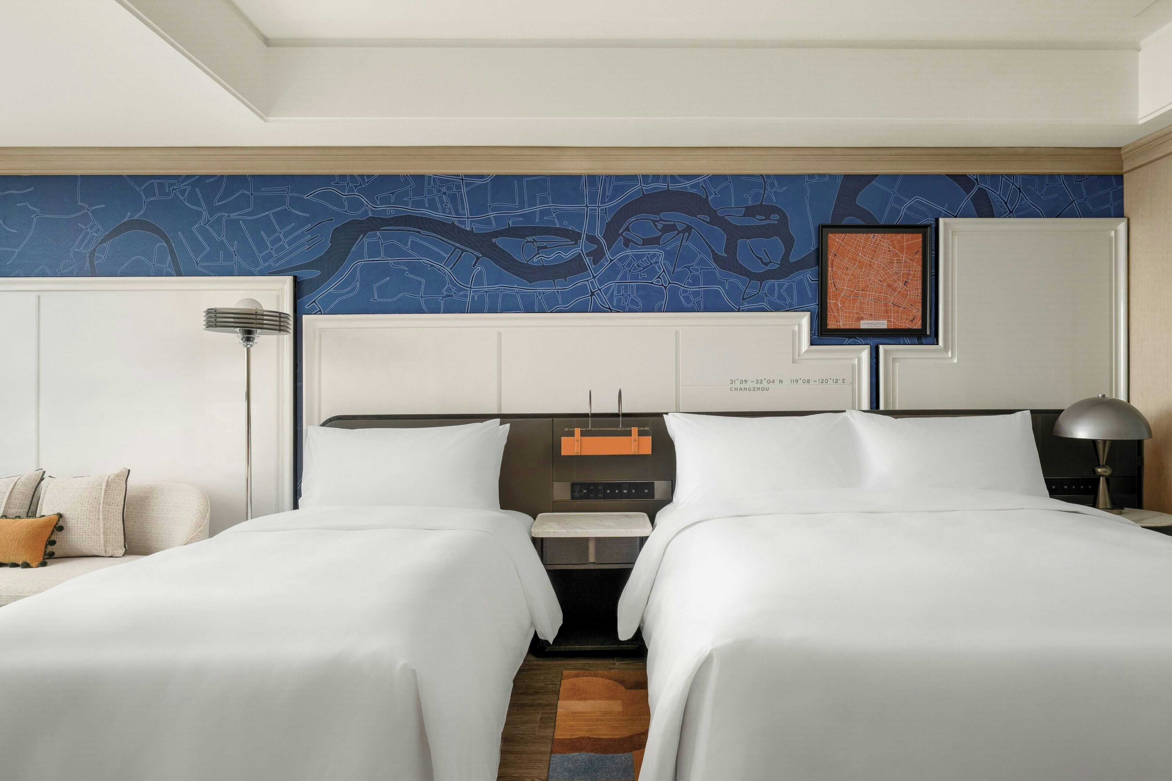 Een hotelkamer met twee bedden, een nachtkastje, een lamp en een wereldkaart aan de muur.