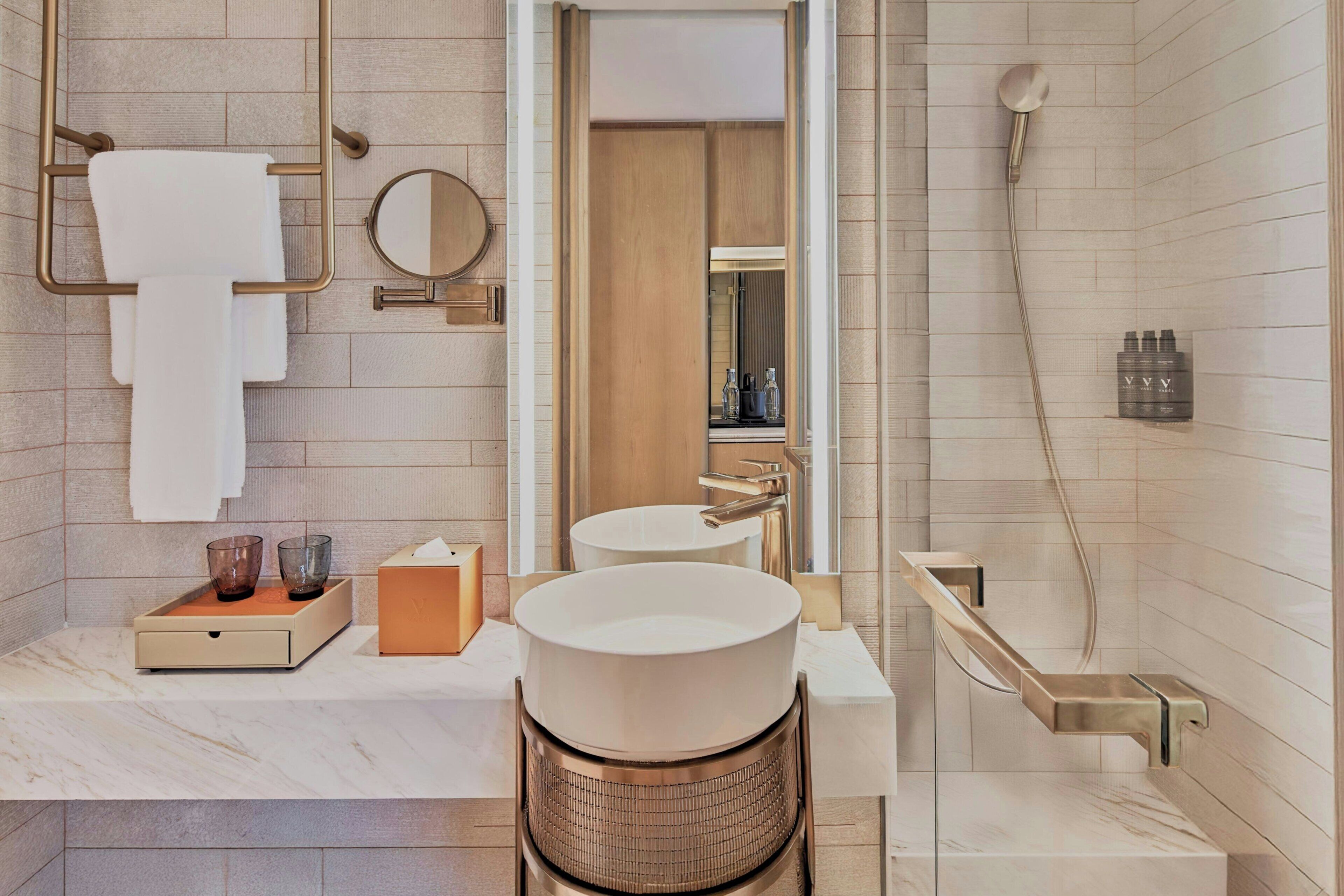 A modern bathroom with a marble countertop, two sinks, a large mirror, a towel rack, a shower, and a toilet.