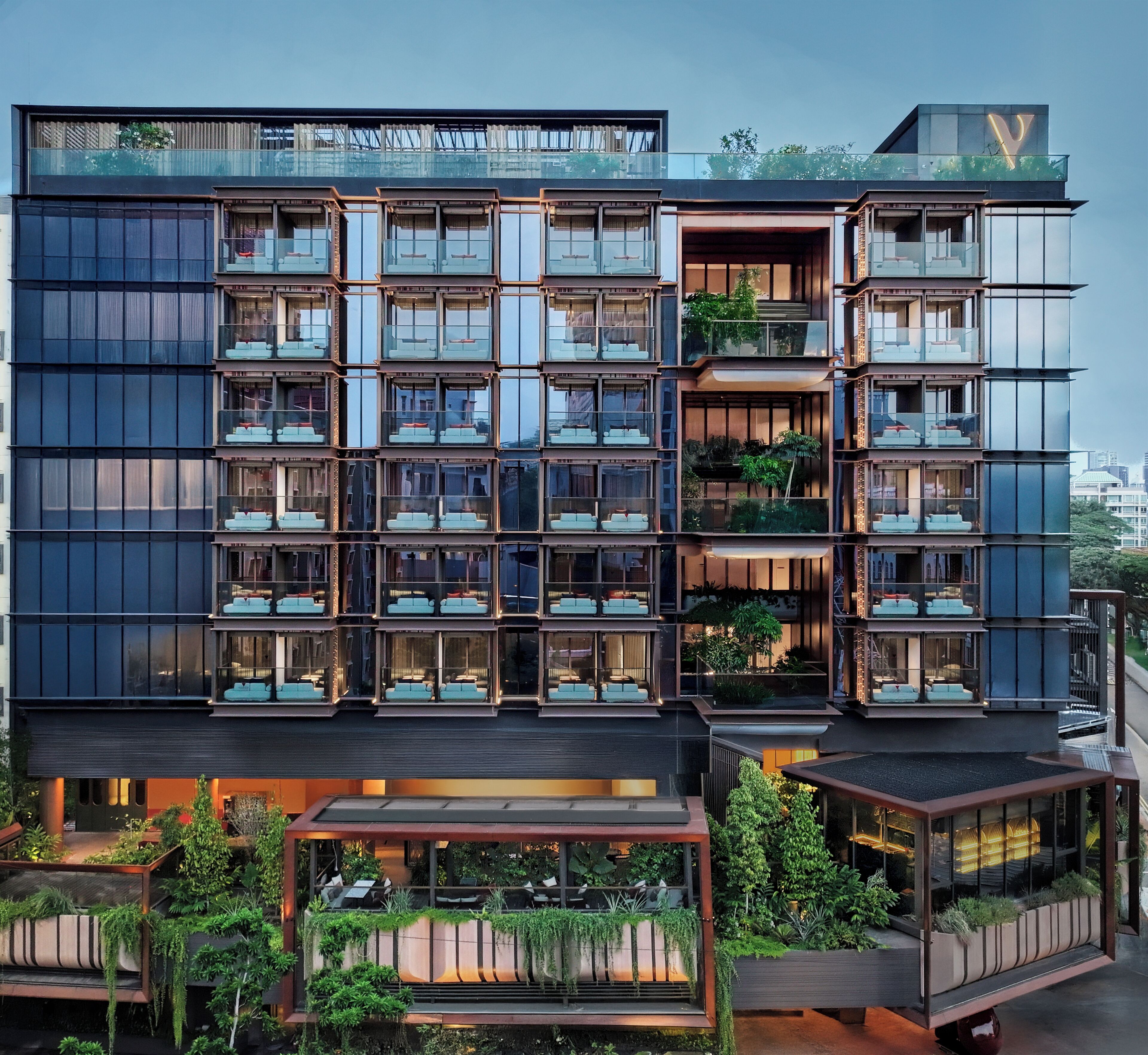 A modern multi-story hotel with balconies, large windows, and indoor plants.