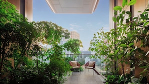 A balcony with plants, two chairs, and a view of the cityscape.