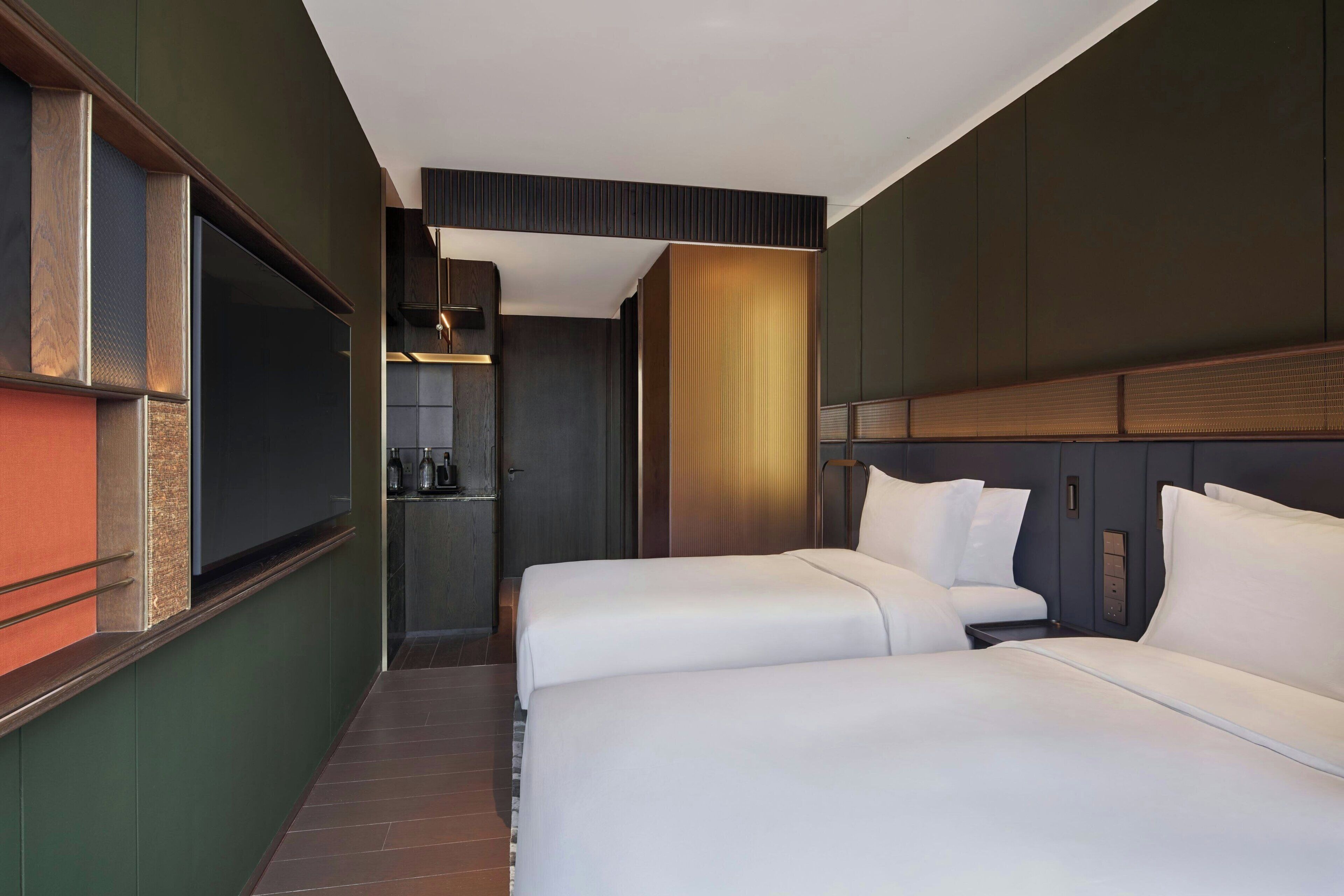A hotel room with two beds, a TV, a minibar, and a bathroom.