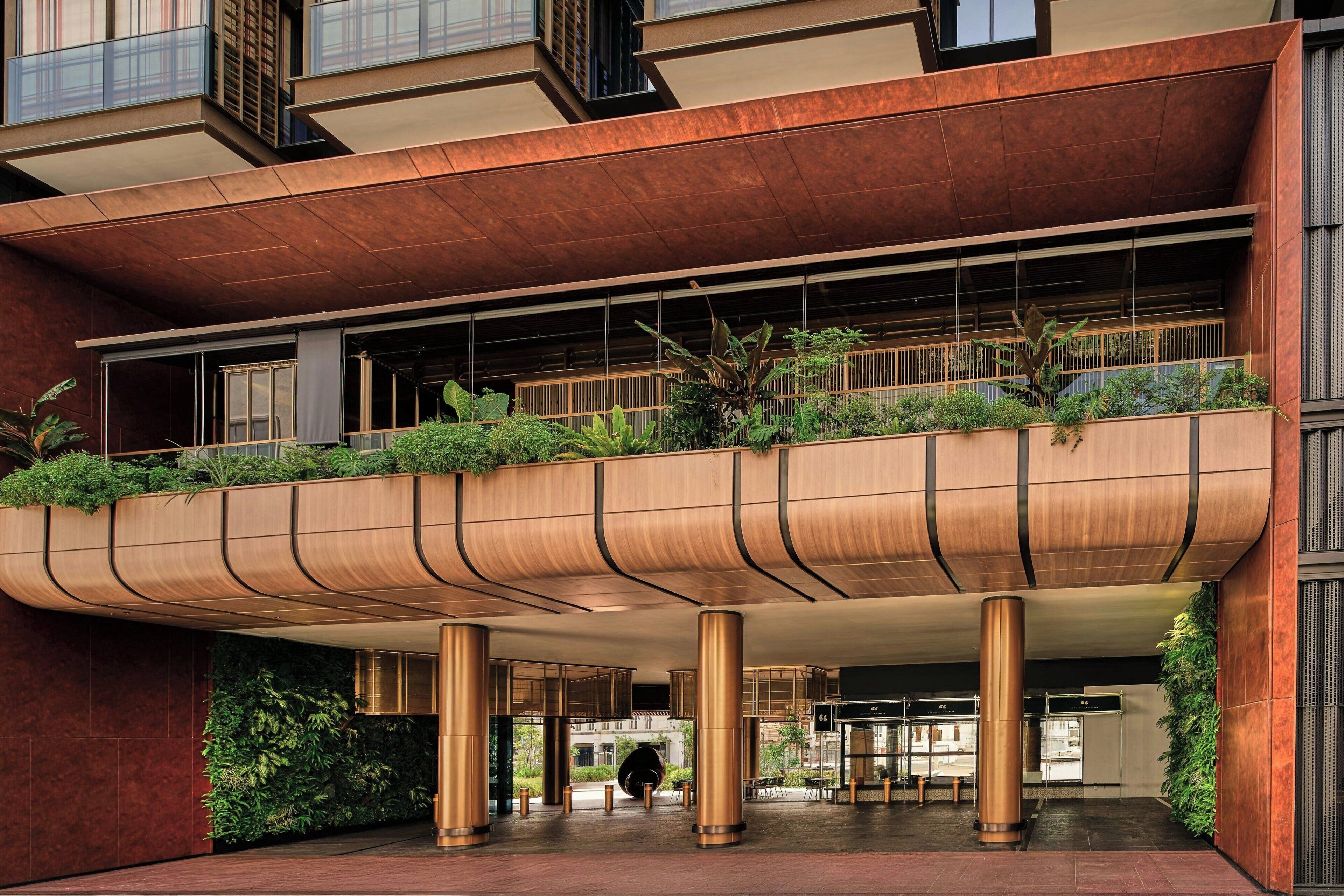 Un edificio moderno con un alero curvo, grandes pilares y un balcón con vegetación.