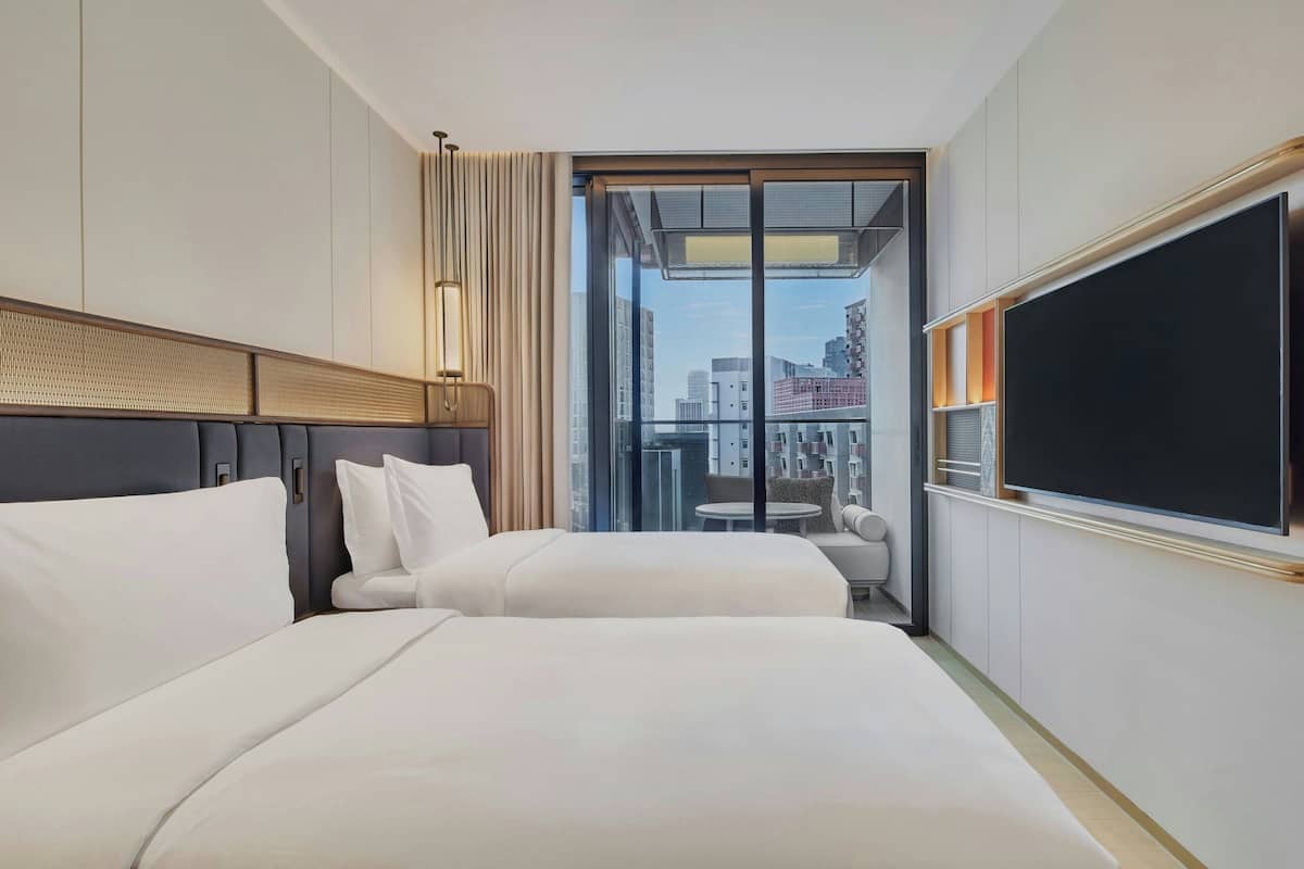A hotel room with two beds, a large window, a flat-screen TV, and a view of the cityscape.