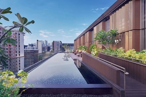 Une piscine à débordement située sur le toit, avec une terrasse en bois, entourée de verdure et offrant une vue panoramique sur la ville.