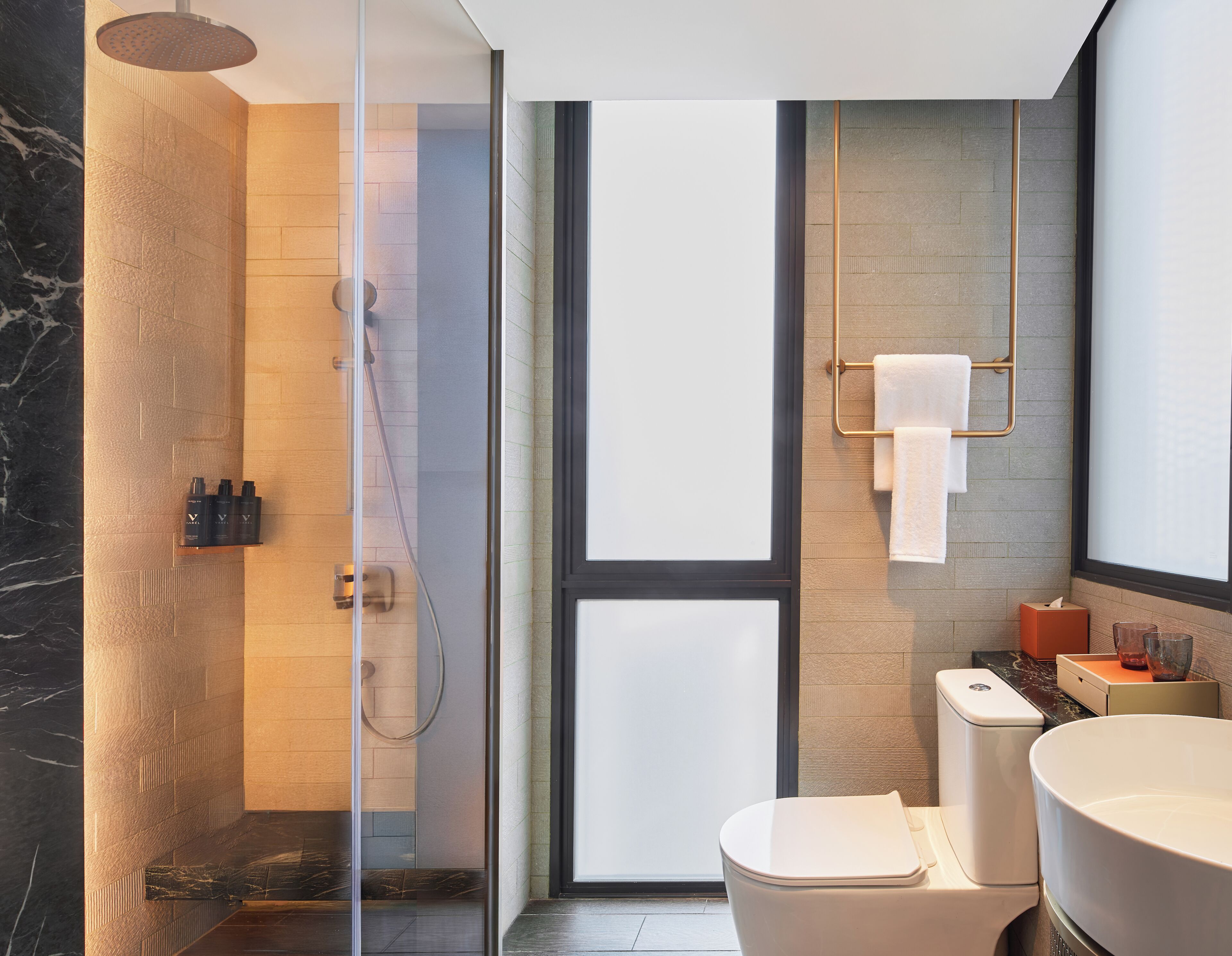 Un baño moderno con ducha envuelta en vidrio, inodoro, lavamanos y toallero.