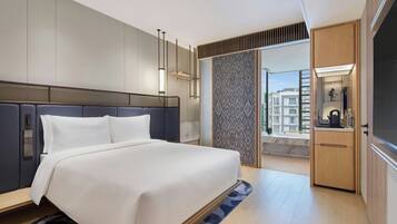 Ein modernes Hotelzimmer mit einem großen Bett, einer integrierten Garderobe, einer kleinen Küchenzeile und Blick auf die Stadtlandschaft.