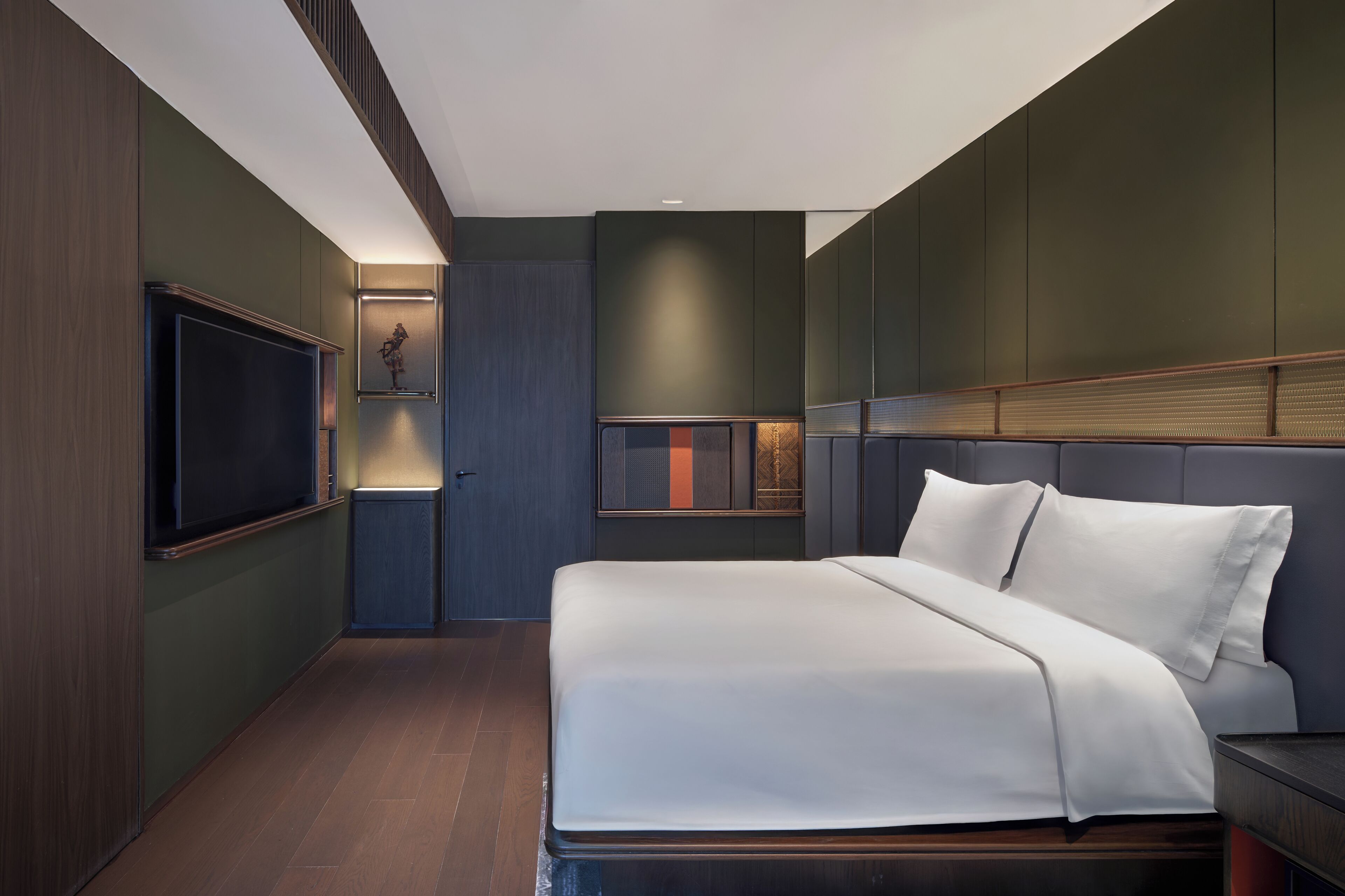 A modern hotel room with a large bed, a flat-screen TV, and a built-in shelf with decorative items.