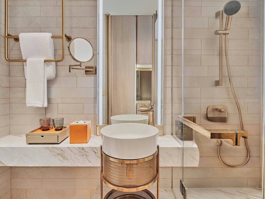 A modern bathroom with a marble countertop, a round mirror, a towel rack, a shower with a handheld showerhead, and a toilet.
