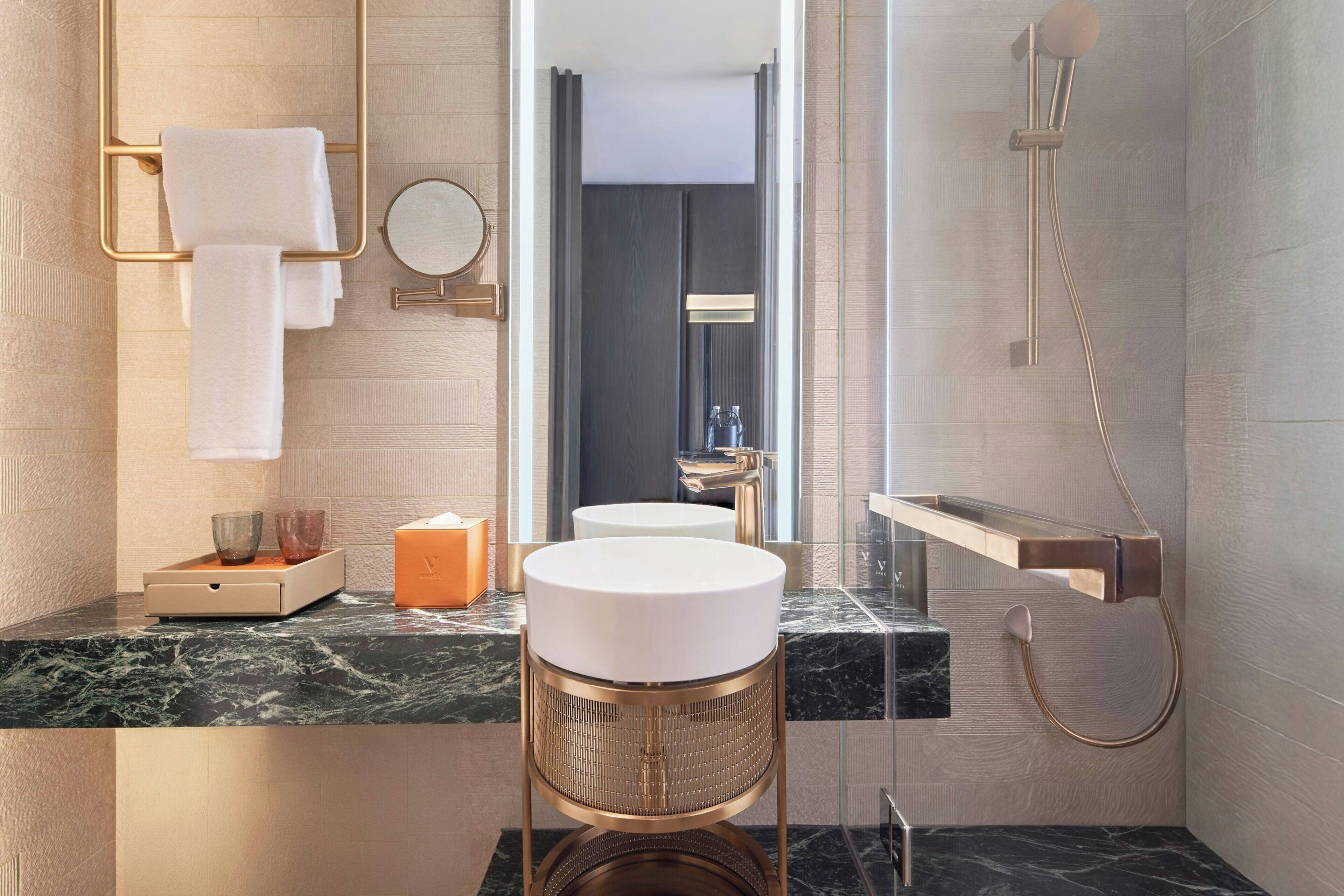 A modern bathroom with a marble countertop, a round sink, a large mirror, a towel rack, and a shower.