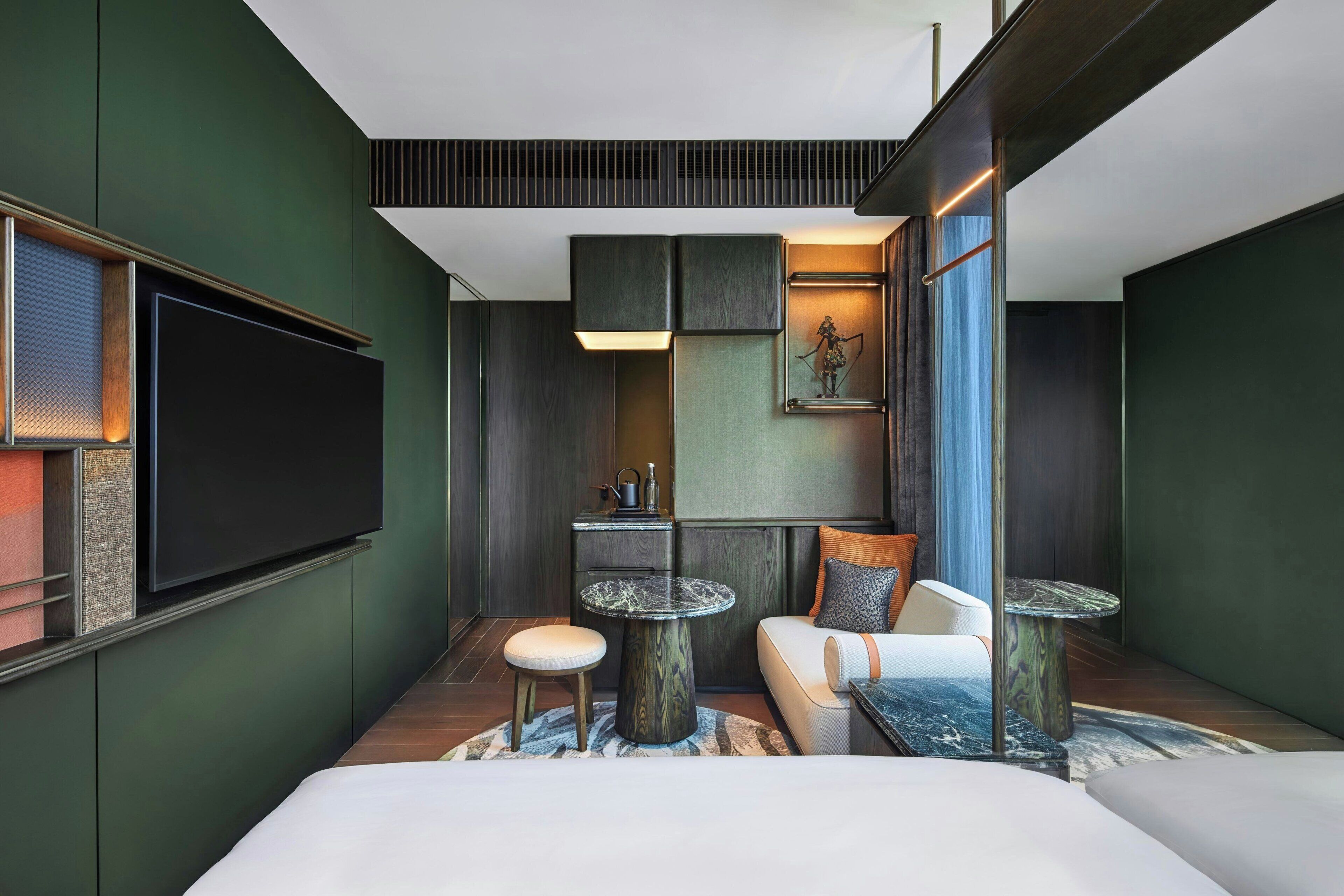 A modern hotel room with a large bed, a flat-screen TV, a small round table, a sofa, and a decorative item on the wall.