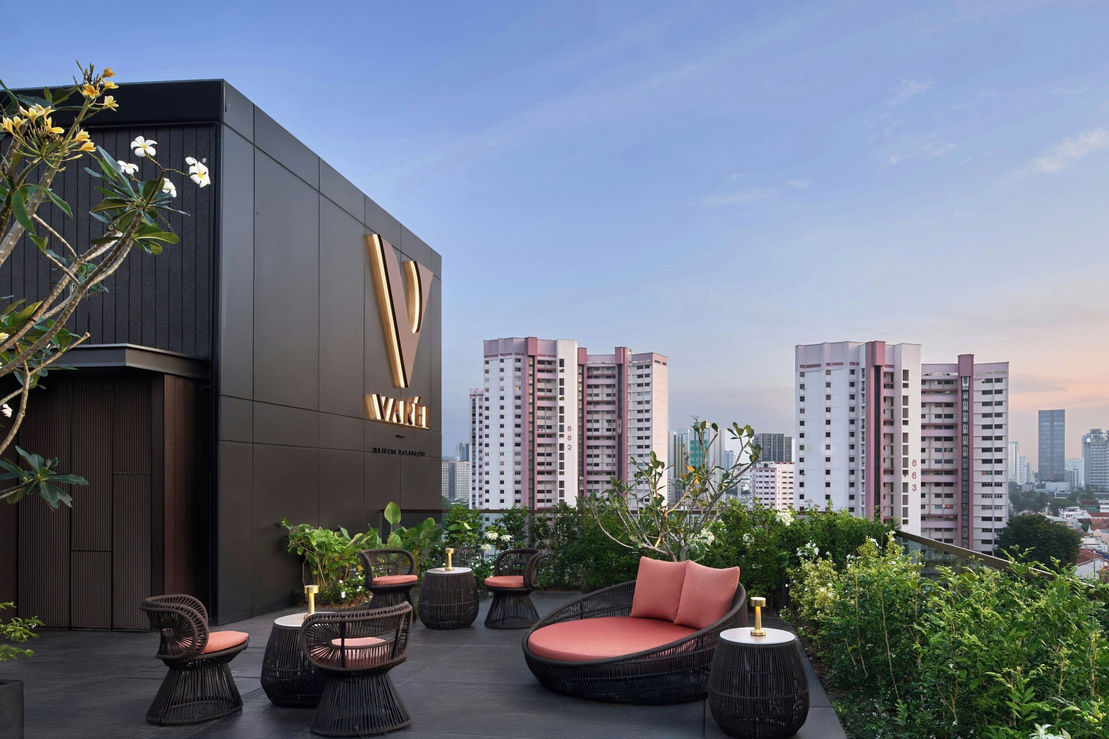 A rooftop lounge with wicker furniture, a modern building facade, and a city skyline in the background.